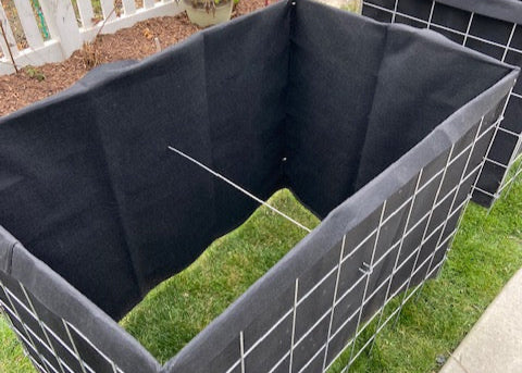 Black fabric lined wire basket planter on grass. 