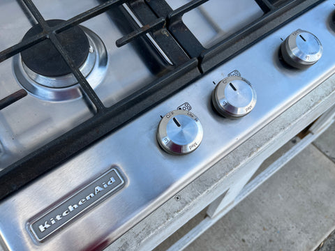 Detail of badge and knobs on good, used KitchenAid 30" gas cooktop. 