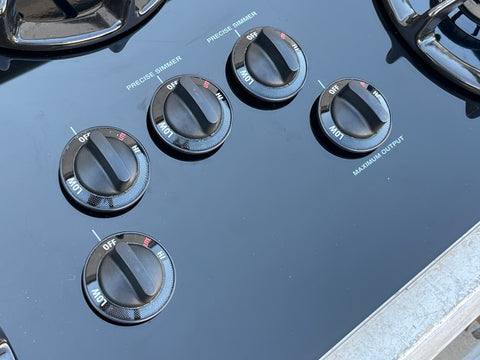 Close up detail of control knobs on G.E. Profile model # JGP636BEV3BB gas cooktop featuring 2 precise simmer burners and one maximum output burner. 