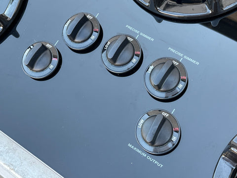 Close up of 5 control knobs on glass surface of GE Profile gas cooktop. 