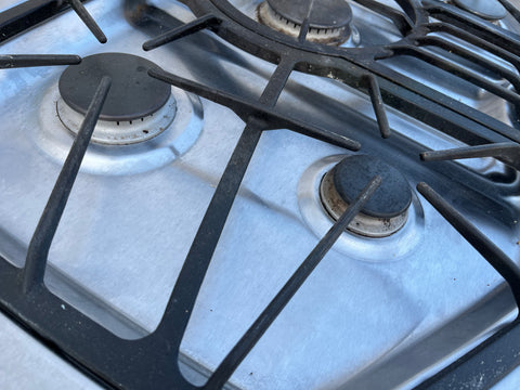 Close-up of left side gas burners and cast iron grates on good used JennAir built-in 36" stovetop. 